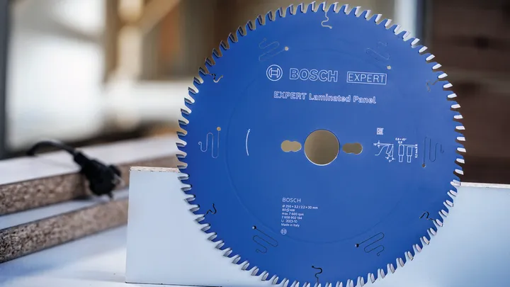 Lama di sega circolare con denti fini appoggiata verticalmente su un banco da lavoro.