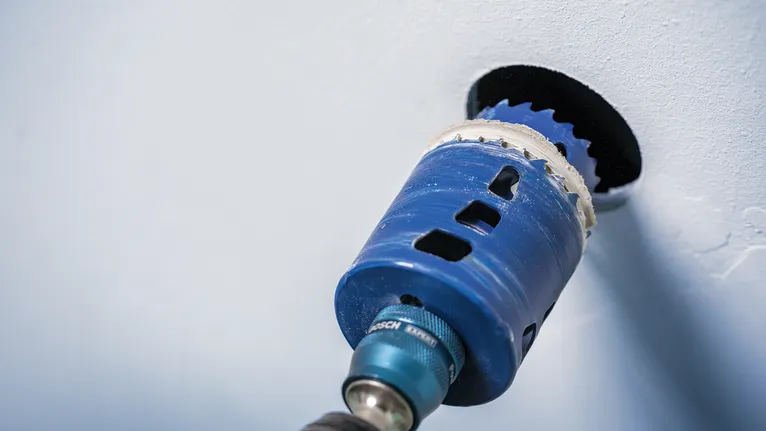 Elettroutensile con sega a tazza che pratica un'apertura circolare in un muro.