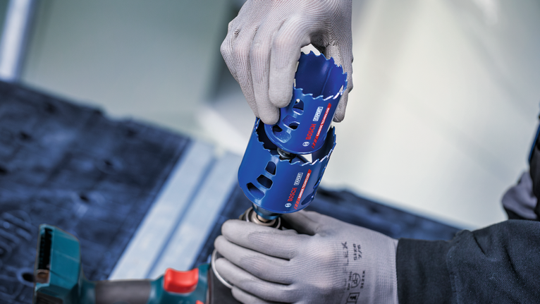 Una persona che indossa un equipaggiamento di sicurezza fissa una sega a tazza blu a un utensile elettrico.