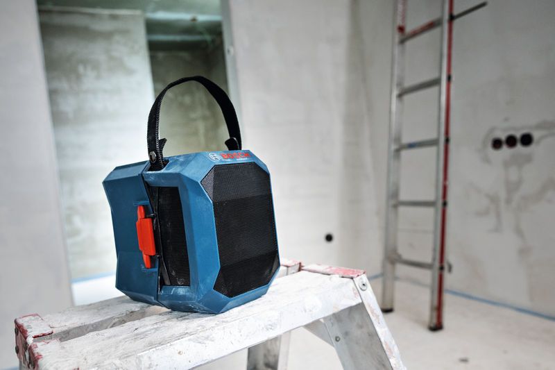 Radio portatile da cantiere con maniglia per il trasporto, posizionata su una scala a pioli in una stanza in costruzione.