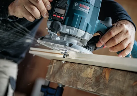 Una persona usa una fresatrice elettrica per rifinire il bordo di una tavola di legno.