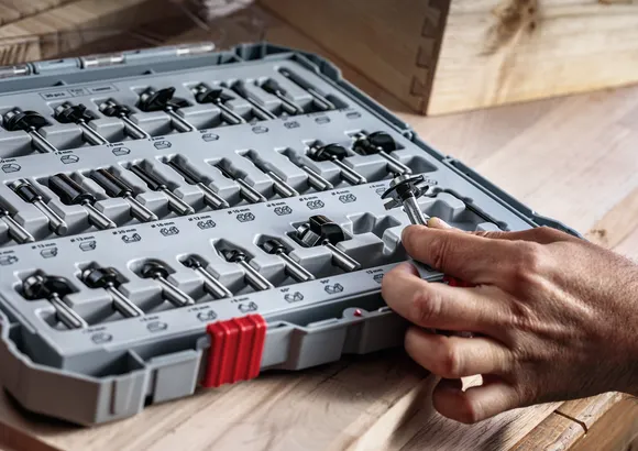 Una persona seleziona una fresa da un set di utensili sistemato su un banco da lavoro in legno.