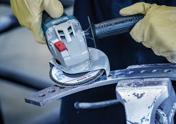 Una persona che indossa un equipaggiamento di sicurezza rettifica una barra di metallo fissata in una morsa.