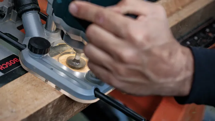 Persona che utilizza una fresatrice per modellare il bordo di una tavola di legno.