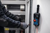 Una persona che indossa un equipaggiamento di sicurezza utilizza un multimetro digitale per controllare un quadro elettrico.