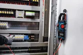 Una persona che indossa un equipaggiamento di sicurezza verifica i collegamenti elettrici utilizzando una pinza amperometrica.