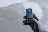 Persona che indossa dispositivi di sicurezza e tiene in mano un misuratore laser su un pavimento di cemento.
