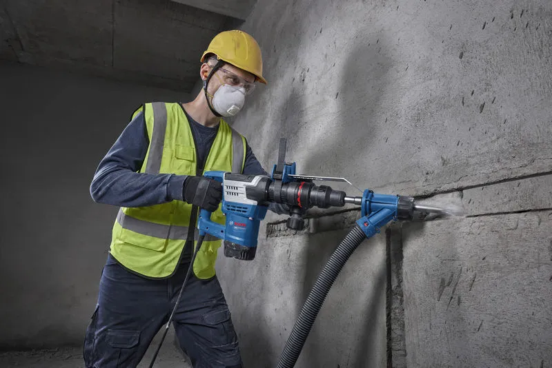 Una persona che indossa un equipaggiamento di sicurezza utilizza un elettroutensile per praticare una scanalatura in un muro di cemento.