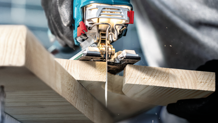 Una persona guida un seghetto alternativo per tagliare un'asse di legno, indossando l'equipaggiamento di sicurezza.