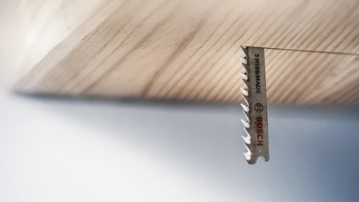 Lama di seghetto alternativo che taglia una tavola di legno dal basso.