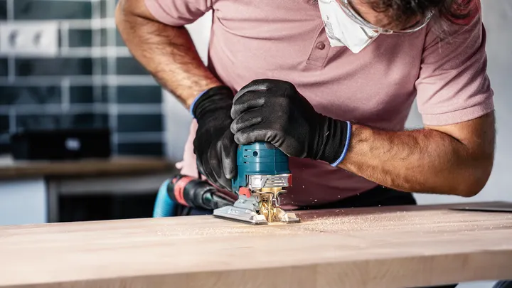 Una persona che indossa un equipaggiamento di sicurezza usa un seghetto alternativo per tagliare la legna.