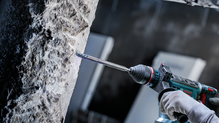 Una persona che indossa un equipaggiamento di sicurezza fora il cemento utilizzando un utensile elettrico.