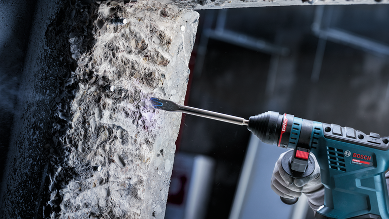 Una persona che indossa un equipaggiamento di sicurezza scalpella il calcestruzzo con un martello perforatore.