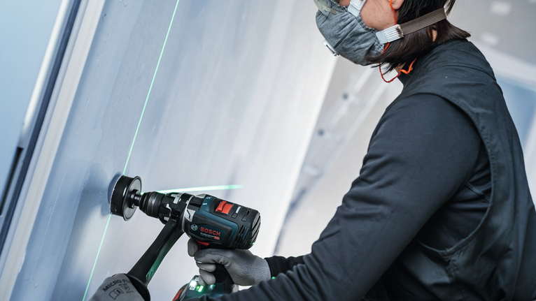 Una persona che indossa un equipaggiamento di sicurezza fora un muro vicino a una guida laser verde.