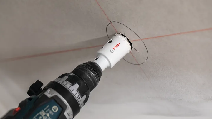 Un trapano elettrico con una sega a tazza pratica un'apertura circolare nel soffitto.