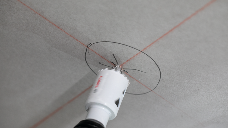 Con una sega a tazza si pratica un'apertura circolare sul soffitto, contrassegnata da linee guida rosse.