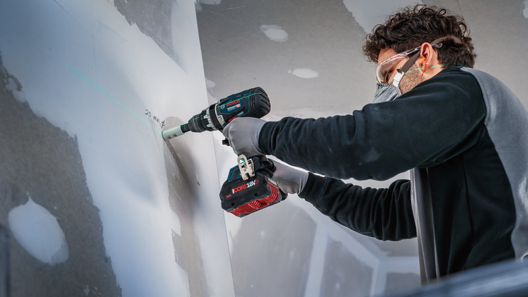 Una persona che indossa l'equipaggiamento di sicurezza pratica un foro nel muro a secco.