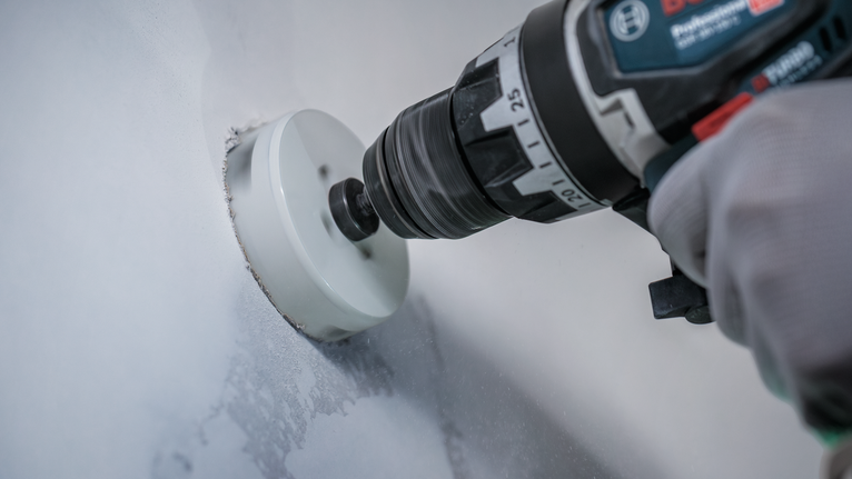 Una persona che indossa un equipaggiamento di sicurezza pratica un grande foro circolare in un muro.