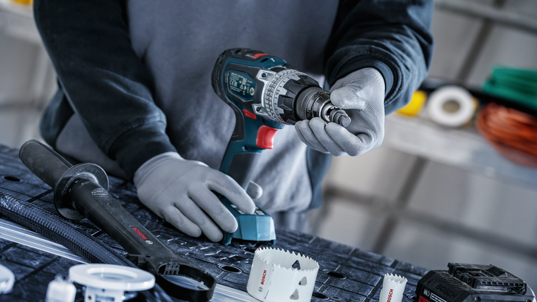 Una persona che indossa un equipaggiamento di sicurezza collega una sega a tazza a un trapano a batteria.