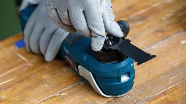 Una persona che indossa un equipaggiamento di sicurezza fissa una lama nera a un elettroutensile.