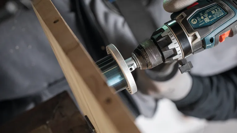 La persona che indossa l'equipaggiamento di sicurezza utilizza un trapano elettrico con una sega a tazza sul legno.