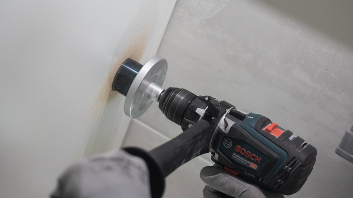 Una persona che indossa un equipaggiamento di sicurezza pratica un foro nel muro con una sega a tazza.