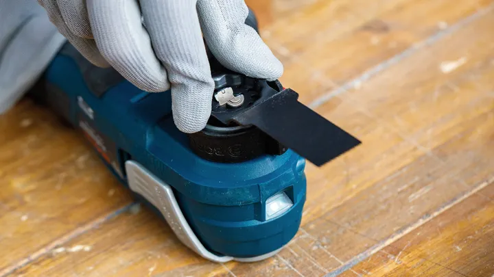 Una persona che indossa un equipaggiamento di sicurezza fissa la lama di un utensile elettrico su una superficie di legno.