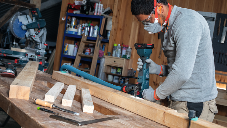 Una persona che indossa l'equipaggiamento di sicurezza fora una trave di legno in un'officina.