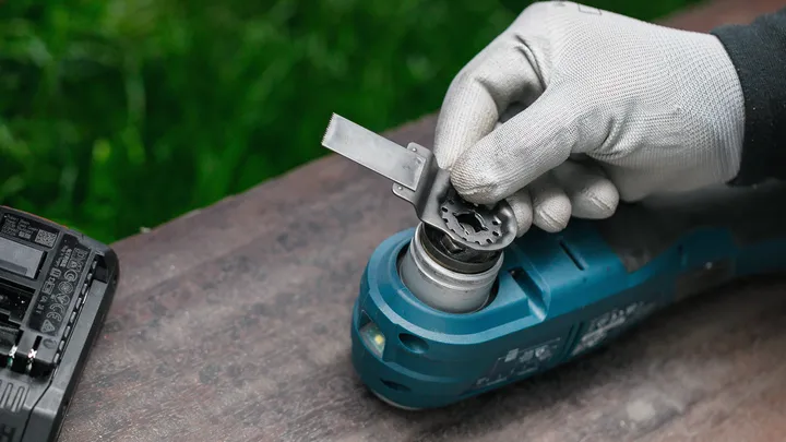 Una persona che indossa un equipaggiamento di sicurezza fissa una lama a un elettroutensile blu.