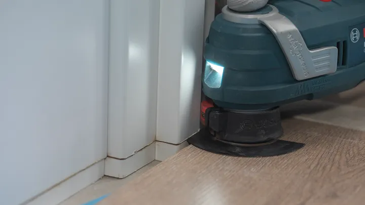 Utensile elettrico con finiture leggere sul pavimento laminato vicino allo stipite di una porta.