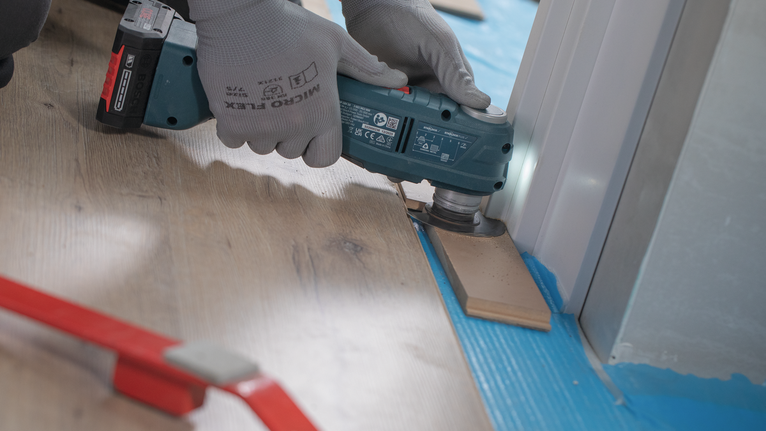 Una persona che indossa dispositivi di sicurezza rifinisce il pavimento laminato vicino allo stipite di una porta.