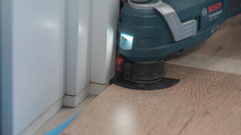 Utensile multiuso oscillante per tagliare pavimenti laminati vicino all'angolo di una parete.