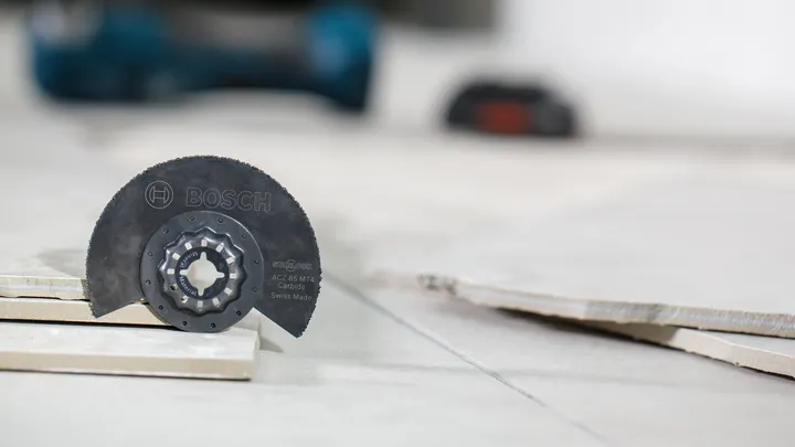 Lama di sega in carburo posizionata tra piastrelle di ceramica impilate su un pavimento piastrellato.