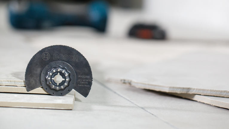 Lama di sega in carburo posizionata tra piastrelle di ceramica impilate su un pavimento piastrellato.