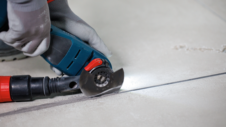 Una persona che indossa un equipaggiamento di sicurezza utilizza un elettroutensile per tagliare una linea retta nelle piastrelle.