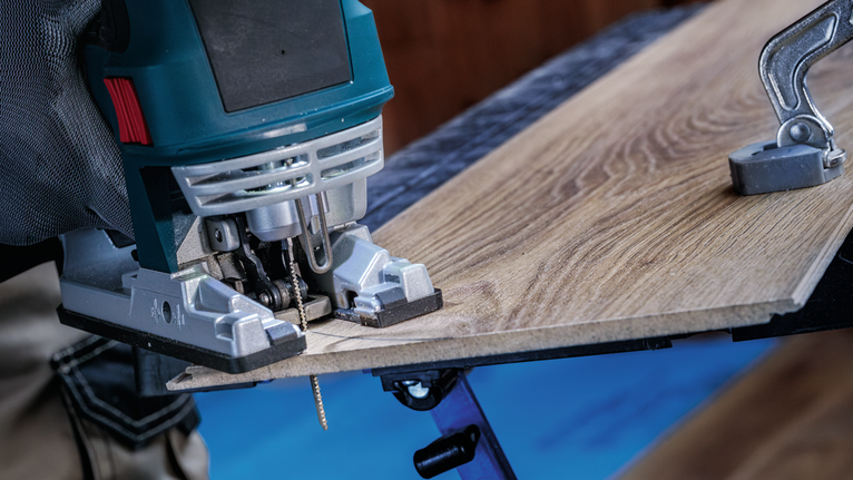 Una persona che indossa un equipaggiamento di sicurezza taglia una tavola di legno con un seghetto alternativo.