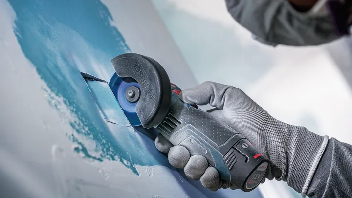 Una persona che indossa un equipaggiamento di sicurezza utilizza una motosega per tagliare il cartongesso.