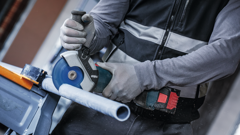 Una persona che indossa un equipaggiamento di sicurezza taglia un tubo di plastica con un elettroutensile.