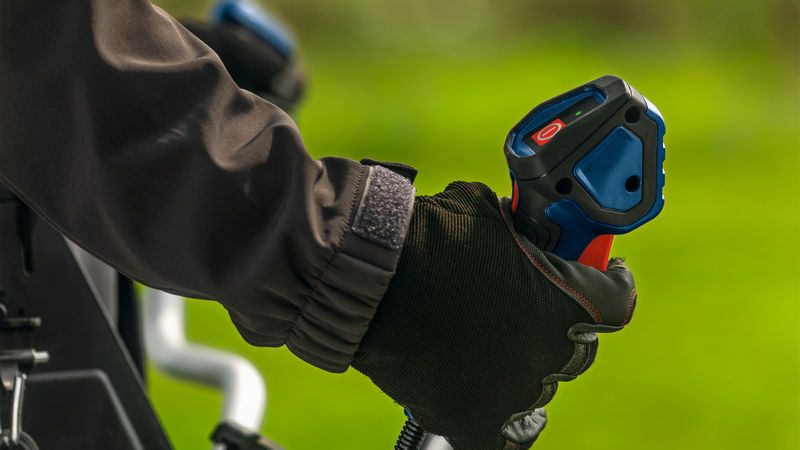 Una persona che indossa un equipaggiamento di sicurezza impugna l'impugnatura di un decespugliatore all'aperto.