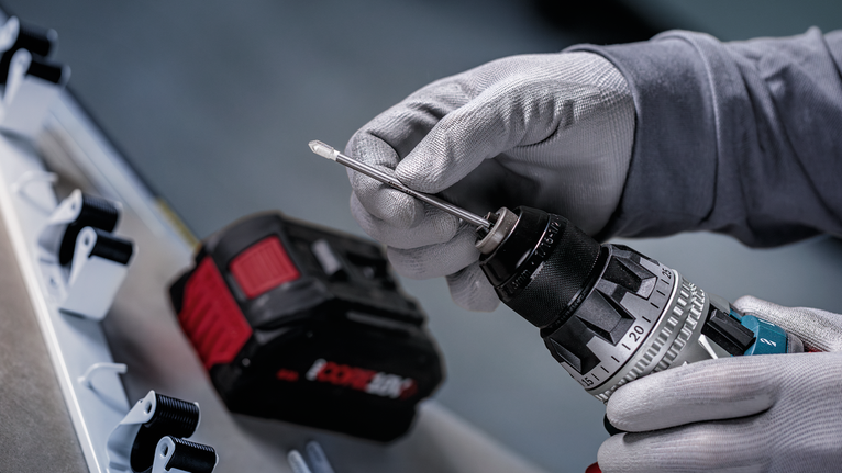 Una persona che indossa un equipaggiamento di sicurezza inserisce una punta da trapano in un trapano a batteria.