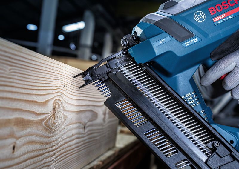 Una persona che indossa un equipaggiamento di sicurezza utilizza una chiodatrice per legno senza fili su una trave di legno.