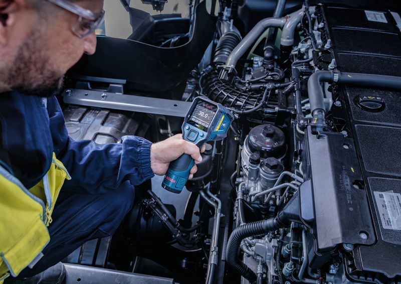 Una persona che indossa dispositivi di protezione individuale utilizza un rilevatore di temperatura per controllare un motore.