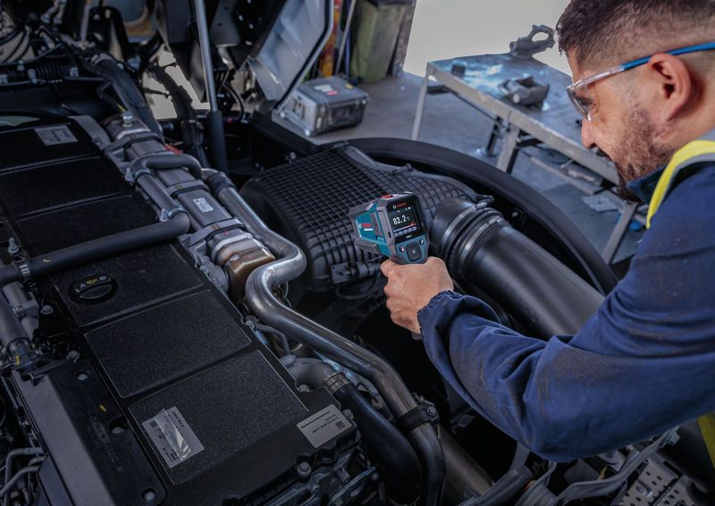 Una persona che indossa dispositivi di protezione individuale utilizza un rilevatore di temperatura per controllare un componente del motore.