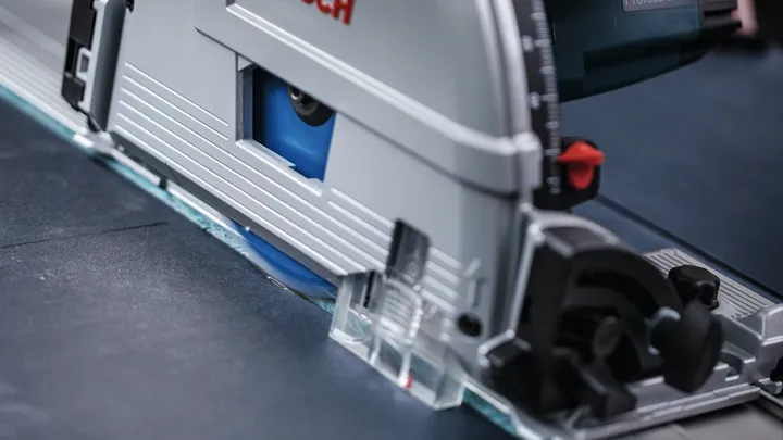 Una sega circolare esegue un taglio preciso attraverso un foglio di materiale scuro.