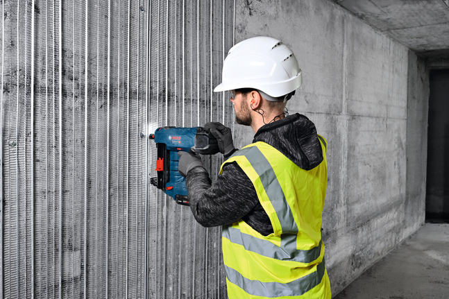 Una persona che indossa un equipaggiamento di sicurezza fissa una rondella metallica universale a un muro di cemento.