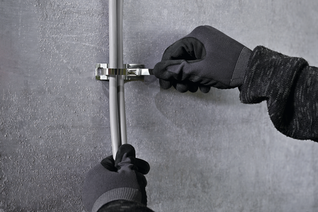 Una persona che indossa un equipaggiamento di sicurezza fissa i cavi a una parete con un supporto per fascette metalliche.