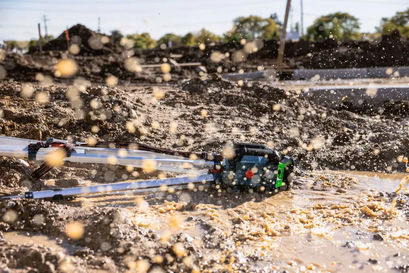 Livella laser abbandonata nel fango bagnato in un cantiere attivo.