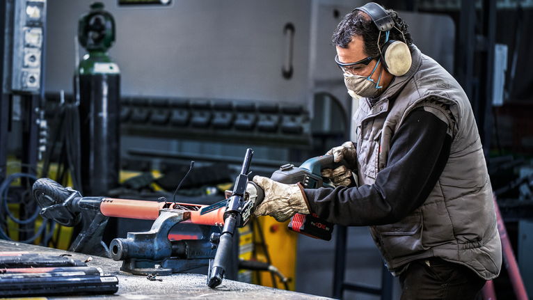 Una persona che indossa un equipaggiamento di sicurezza aziona un elettroutensile su un tubo metallico bloccato.