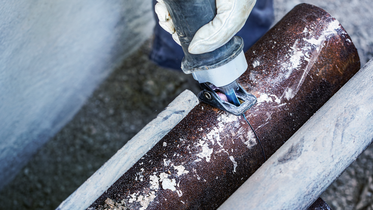 Una persona che indossa un equipaggiamento di sicurezza utilizza un elettroutensile per tagliare un tubo metallico.