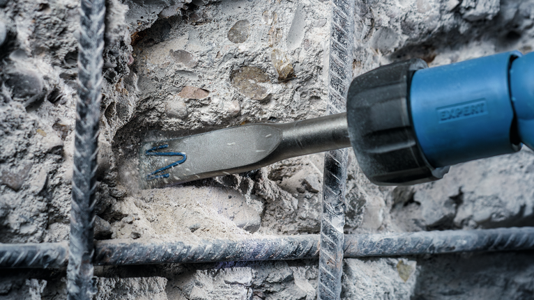 Utensile scalpellatore che rompe il calcestruzzo tra le barre di rinforzo metalliche.